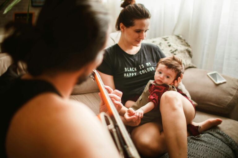 Anonymous father playing guitar on couch for baby and wife