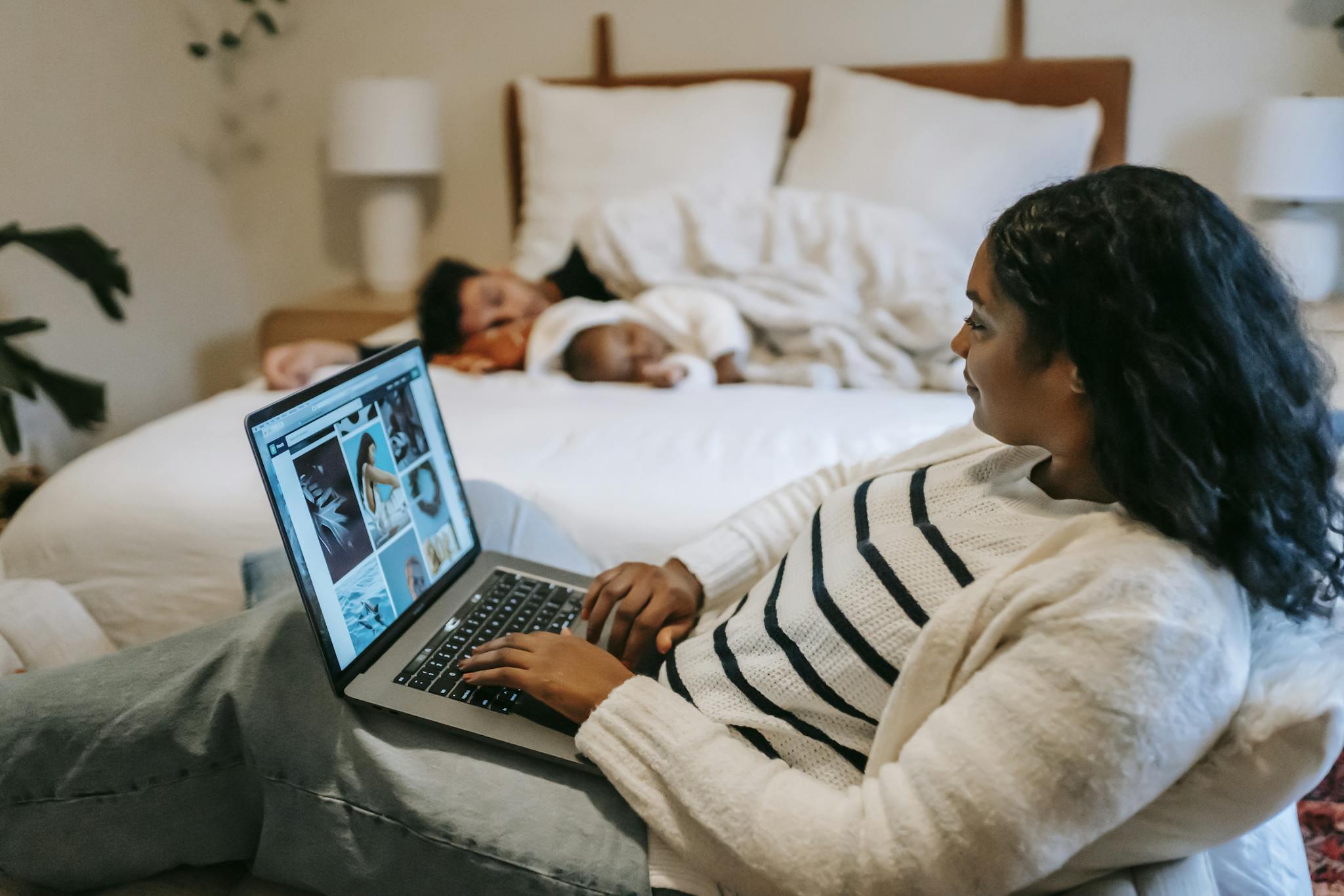 Ethnic mother using laptop near baby sleeping on bed with father